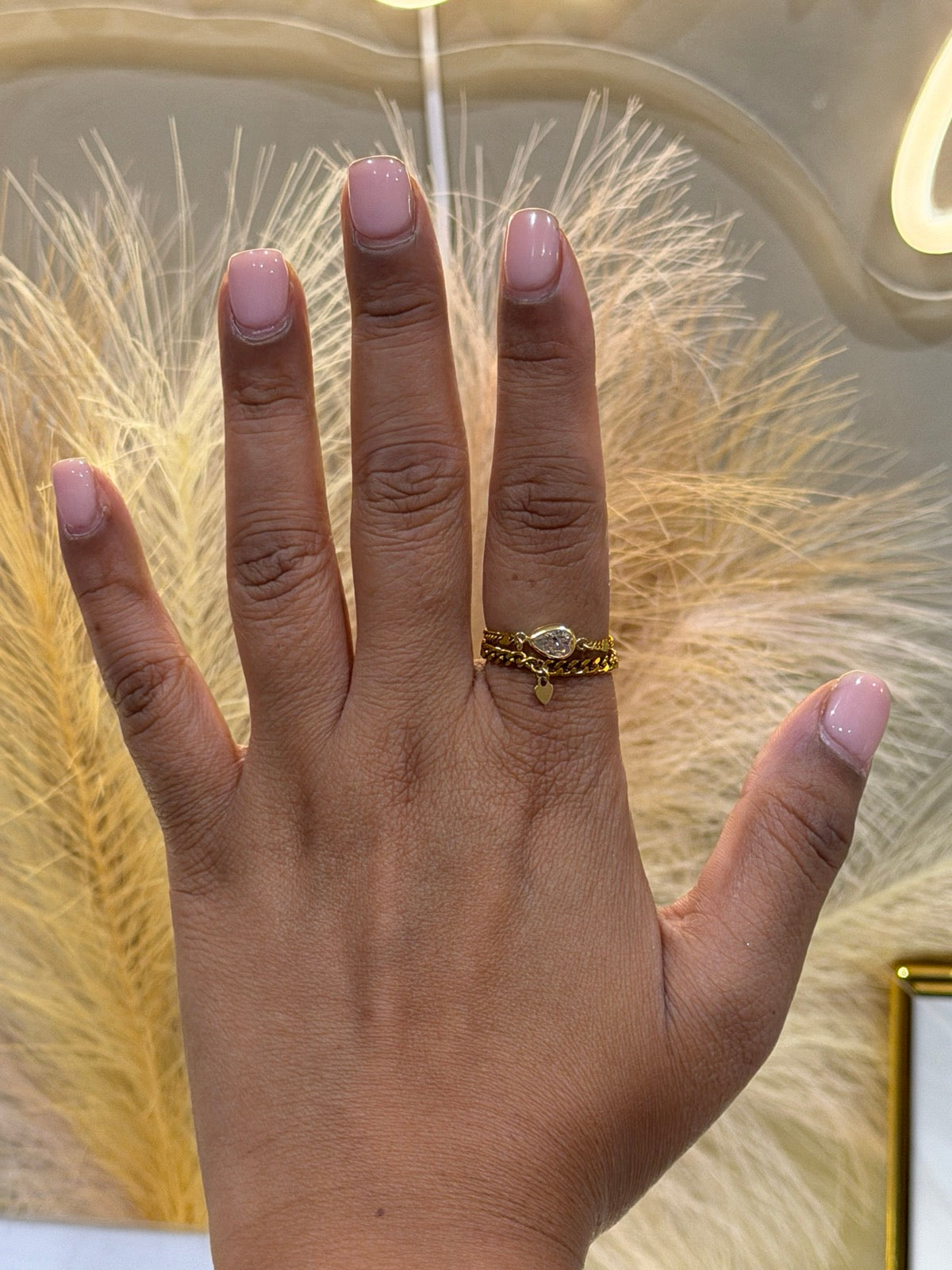 The Molly ring stack, two gold chain rings worn together, one set with a teardrop stone and one with a small heart charm
