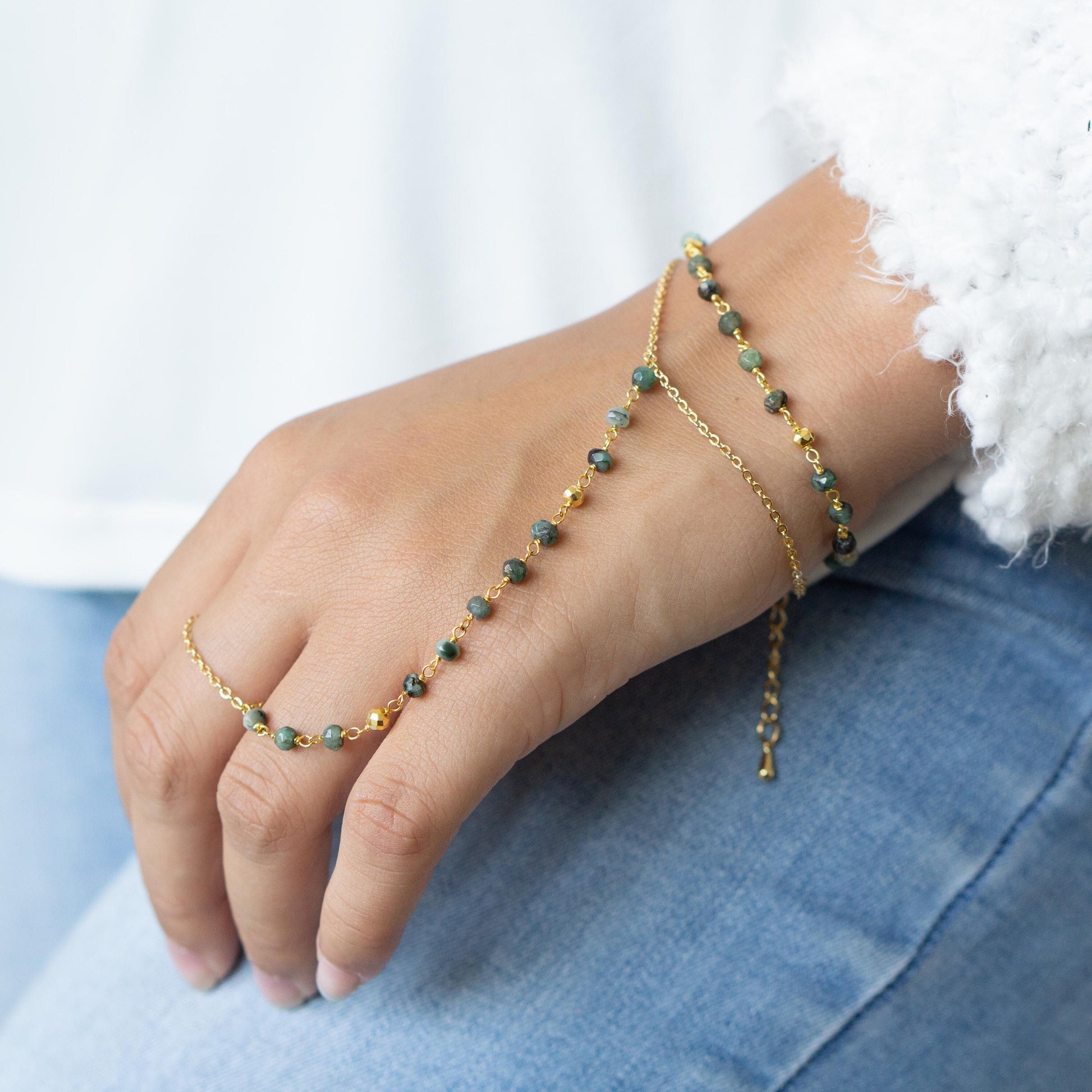 a womans hand with a gold chain bracelet and a green beaded bracelet Travelers emerald hand chain bracelet Explorers gold filled gemstone bracelet