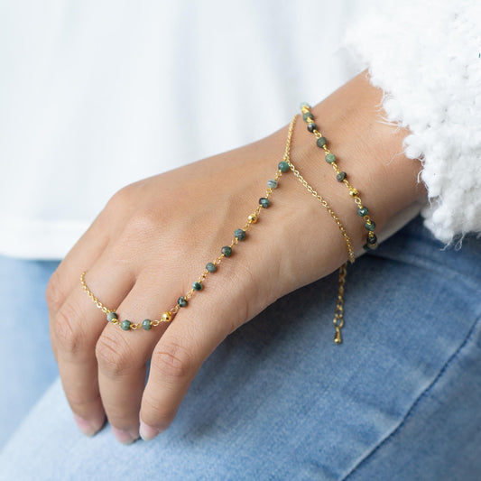 a womans hand with a gold chain bracelet and a green beaded bracelet Travelers emerald hand chain bracelet Explorers gold filled gemstone bracelet